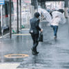 台風の中、傘をさして歩く男性