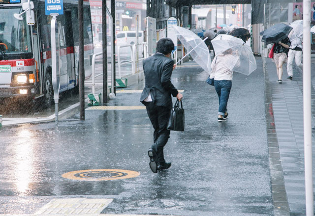 台風の中、傘をさして歩く男性